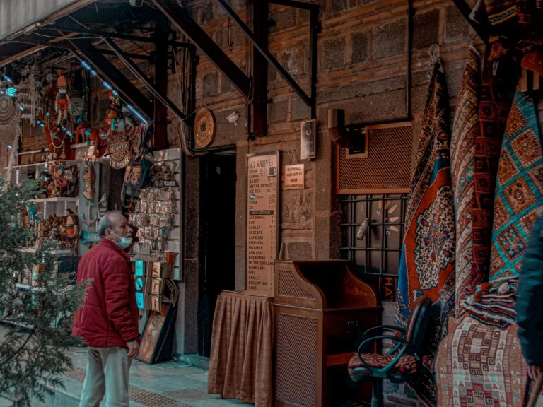 Senior male customer in mask standing at local street market selling carpets and various oriental souvenirs